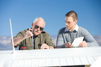 Image of a teacher demonstrating a task to a student by the wing of a plane